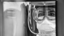 nurse in PPE looks through window