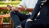 two people sitting on bench looking at tablet