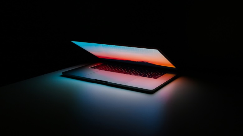 half open laptop in dark room with multicolored screen