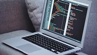 Laptop open on arm of gray couch Laptop open on arm of gray couch