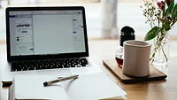 Laptop open on desk beside notebook and mug Laptop open on desk beside notebook and mug
