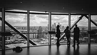 Three people standing in front of wall of windows Three people standing in front of wall of windows