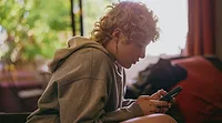 Teenager with blonde curly hair texting on their cell phone Teenager with blonde curly hair texting on their cell phone