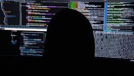 Person in black hooded sweatshirt staring at multiple computer screens