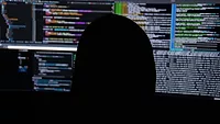 Person in black hooded sweatshirt staring at multiple computer screens