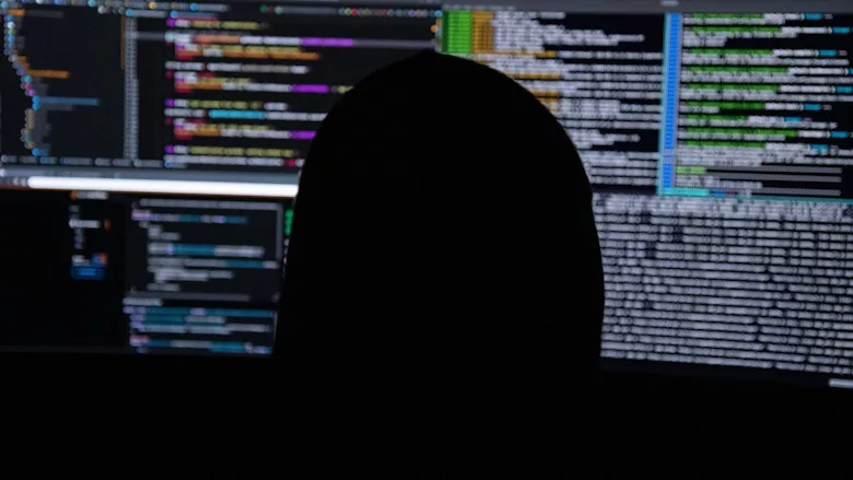 Person in black hooded sweatshirt staring at multiple computer screens
