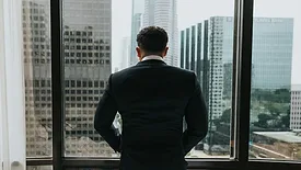 Man in suit looking out window at city 