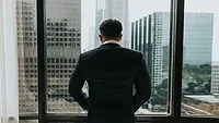 Man in suit looking out window at city 