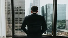 Man in suit looking out window at city 