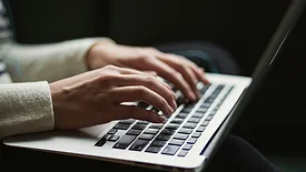 Person in white sweater working on laptop