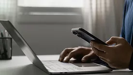 Person working on laptop with cell phone