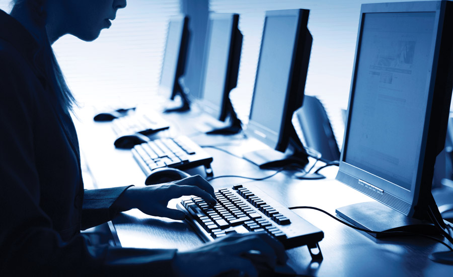 Woman sitting in a darkened room using a computer and looking at the screen.